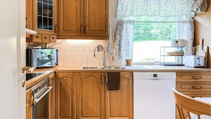 Eine kompakte Küche mit Holzausstattung, Backofen, Geschirrspüler und einem Fenster mit Vorhängen.