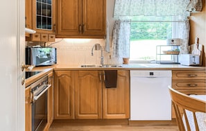 A compact kitchen with wooden cabinets, a built-in oven, a dishwasher, and a window with curtains. - 5 bedroom lovely home in Syvde (Syvde)