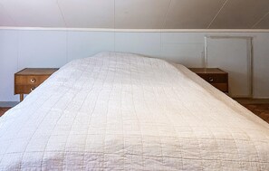 A bed with a quilted cover in a room with a plain wall and two wooden nightstands. - 5 bedroom lovely home in Syvde (Syvde)