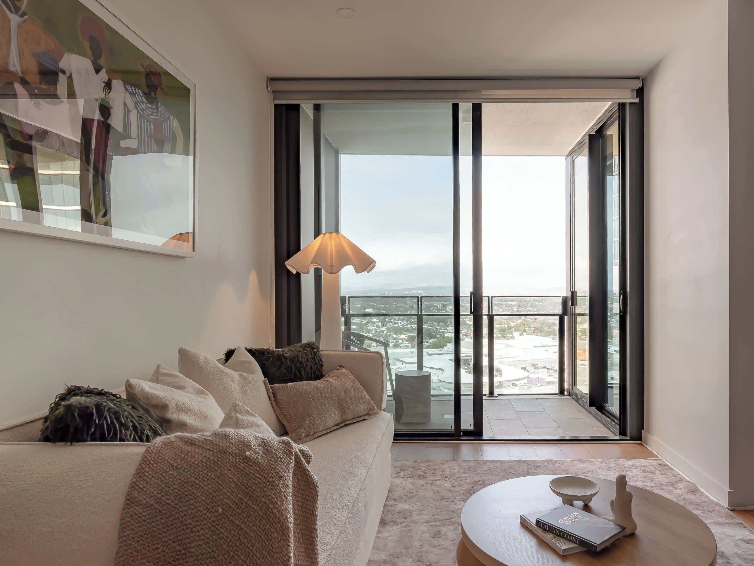 A modern living room with a sofa, a coffee table, and a large window offering a city view.