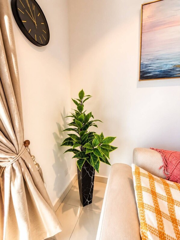 Un rincón de una habitación con un reloj negro, una planta en maceta, un sofá y un cuadro en la pared.