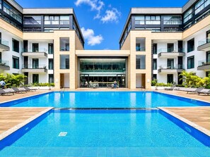 Un hotel moderno con piscina central, varios balcones y fachada de vidrio.