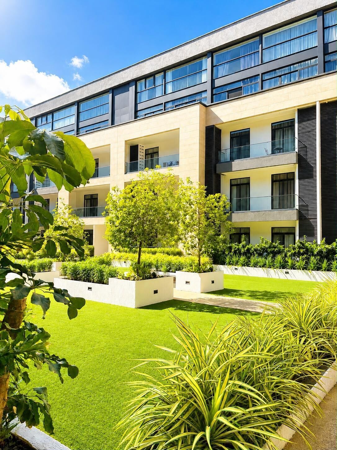 Un bâtiment moderne doté de nombreux balcons, d’un jardin bien entretenu et surplombant un ciel d’un bleu éclatant.