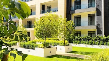Un bâtiment moderne doté de nombreux balcons, d’un jardin bien entretenu et surplombant un ciel d’un bleu éclatant.