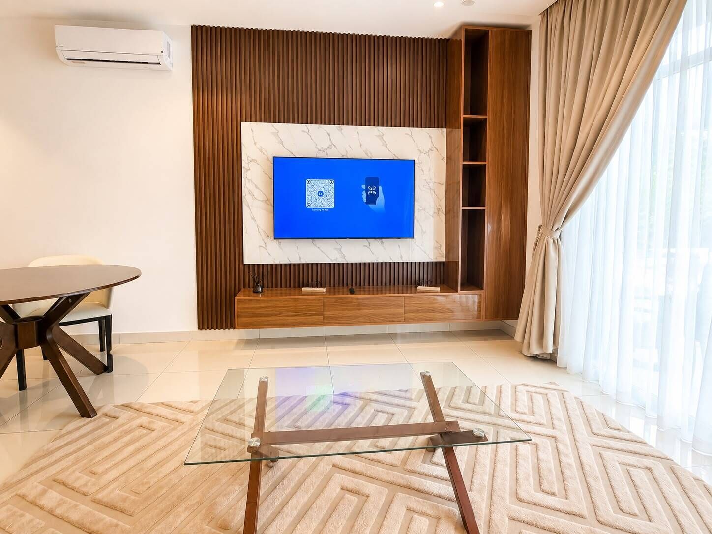 Una sala de estar moderna con un televisor de pantalla plana montado en una pared de mármol, una mesa de centro de vidrio y un mueble de entretenimiento de madera.