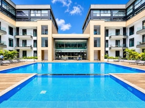 Ein modernes Hotel mit einem zentral gelegenen Schwimmbad, mehreren Balkonen und einer Glasfassade.