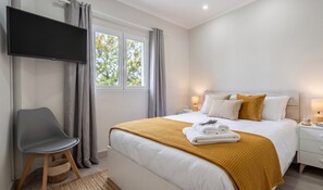 A modern hotel room with a bed, a chair, a TV, and a window with curtains. - Azores Green Escape (Povoação)