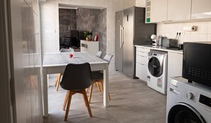 A modern kitchen with a dining area, a washing machine, and a refrigerator. - Azores Green Escape (Povoação)