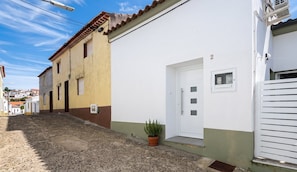 A narrow street with buildings on either side, a door with a window, and a potted plant on the ground. - Azores Green Escape (Povoação)