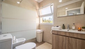 A modern bathroom with a toilet, bidet, and sink. There is a window with a view of greenery outside. - Azores Green Escape (Povoação)