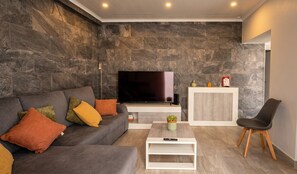 Een moderne woonkamer met een grijze bank, een flatscreen televisie, een witte salontafel en een houten stoel.