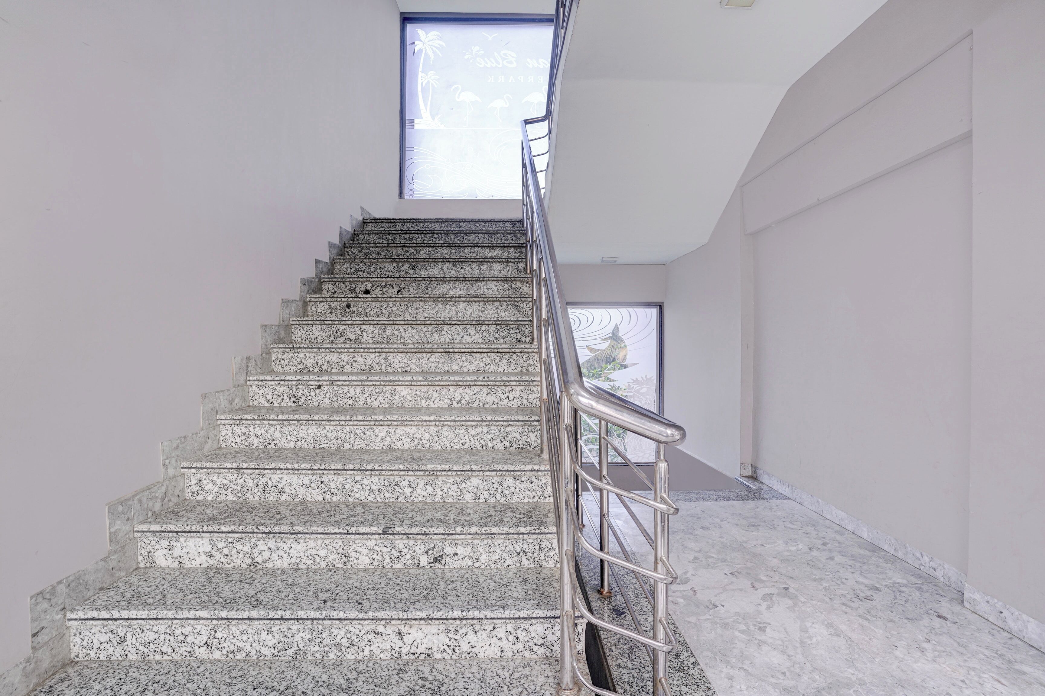 Una escalera con barandilla de metal que lleva a una plataforma, una ventana con vistas y una pared lisa.