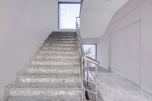 Un escalier avec une rampe métallique menant à un palier, une fenêtre offrant une vue et un mur sobre.