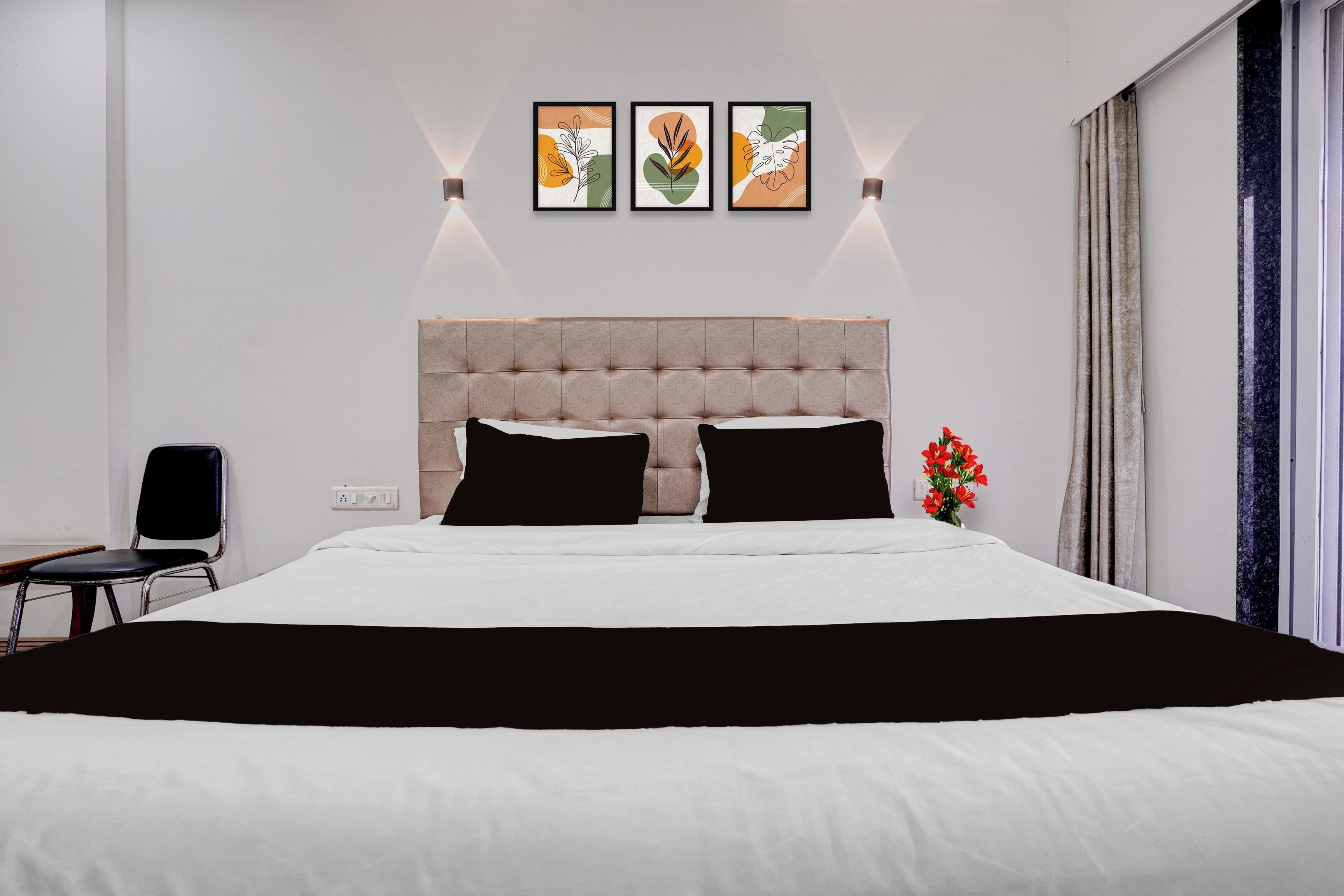 Una habitación de hotel moderna con una cama grande, una silla, una mesita de noche y una ventana con cortinas.