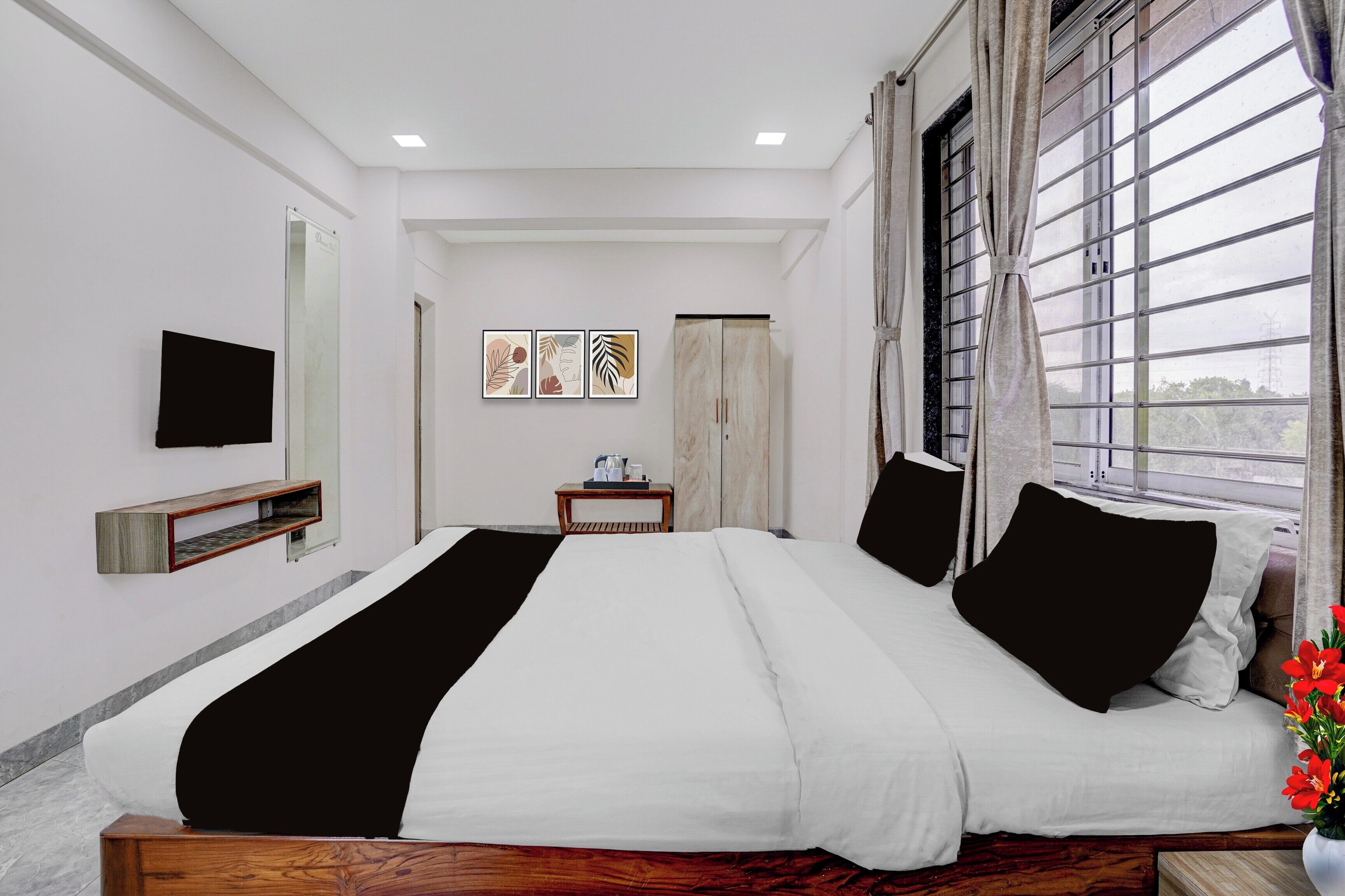 A hotel room with a large bed, a flat-screen TV, a small table with a lamp, and a window with curtains.