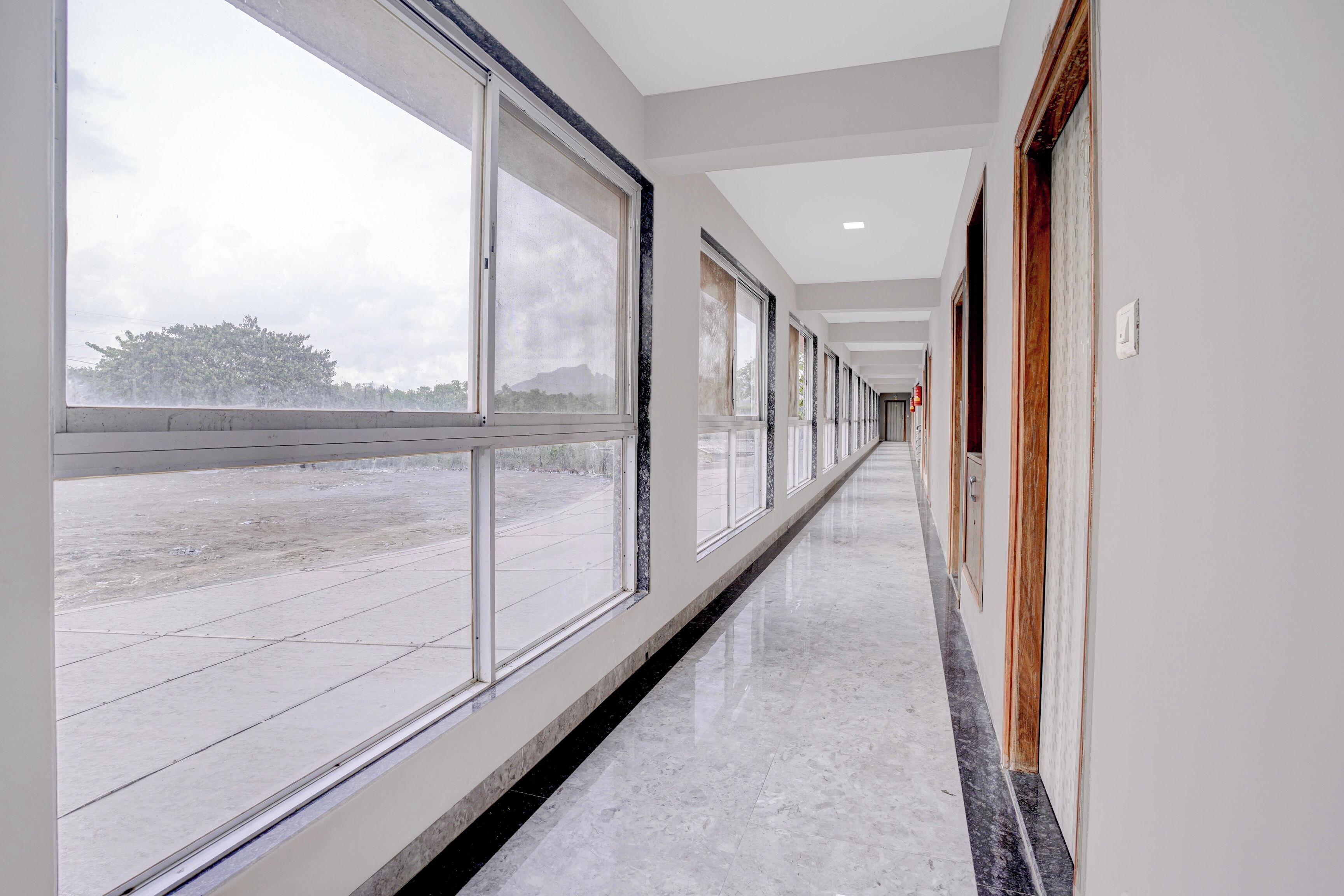 A long, narrow hallway with large windows on one side and doors on the other, leading to a room.