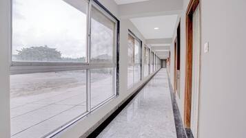 A long, narrow hallway with large windows on one side and doors on the other, leading to a room.