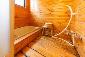 Ein Badezimmer in einer Holzhütte mit einer Badewanne, einem kleinen Holzschemel und einem Duschschlauch.