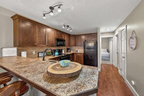 A kitchen with wooden cabinets, granite countertops, a built-in microwave, and a refrigerator. - Mountain Hearth - a RidgeView Resort Partner Property (Radium Hot Springs)