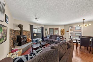 A living room with a stone fireplace, a sofa set, a dining area with chairs, and a television on a stand. - Mountain Hearth - a RidgeView Resort Partner Property (Radium Hot Springs)