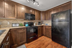 Una cocina con armarios de madera, un refrigerador negro, un microondas y una estufa.