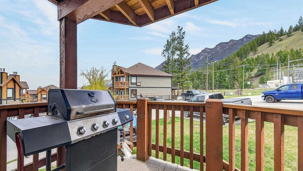 A barbecue grill on a balcony with a view of houses and mountains. - Mountain Hearth - a RidgeView Resort Partner Property (Radium Hot Springs)