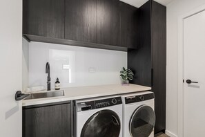 Een kleine wasruimte met een wasmachine, een wasbak en een plantje.