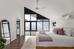 Ein modernes Schlafzimmer mit einem großen Bett, einem Deckenventilator, Blick durch eine Schiebetür und Holzboden.