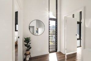 Ein Flur mit einem runden Spiegel, einer Zimmerpflanze und Blick durch ein Fenster mit Jalousien.