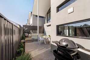 Een modern buitenterras met een barbecue, een zithoek met een tafel en stoelen, en uitzicht op een woongebouw met grote ramen.