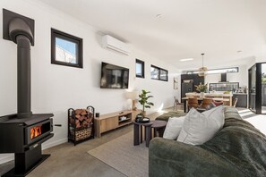 Ein modernes Wohnzimmer mit Kamin, Fernseher und Essbereich, im Hintergrund eine Küche.