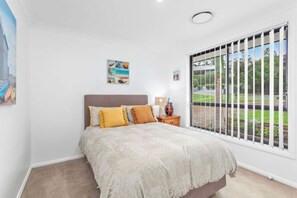 A bedroom with a bed, a nightstand, a lamp, and a window with a view of greenery.