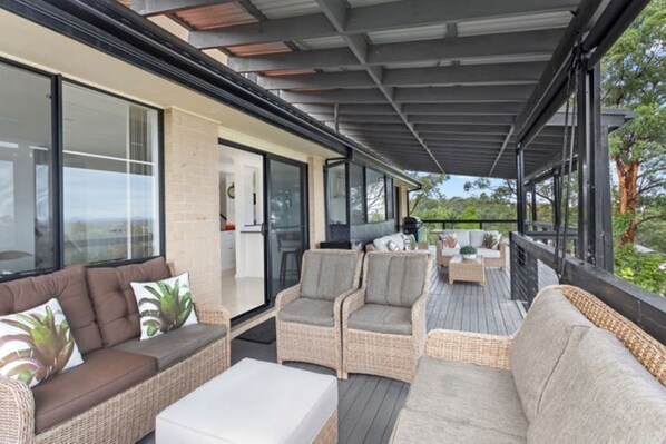 An outdoor covered patio with wicker furniture, a white table, and a view of the surrounding landscape.