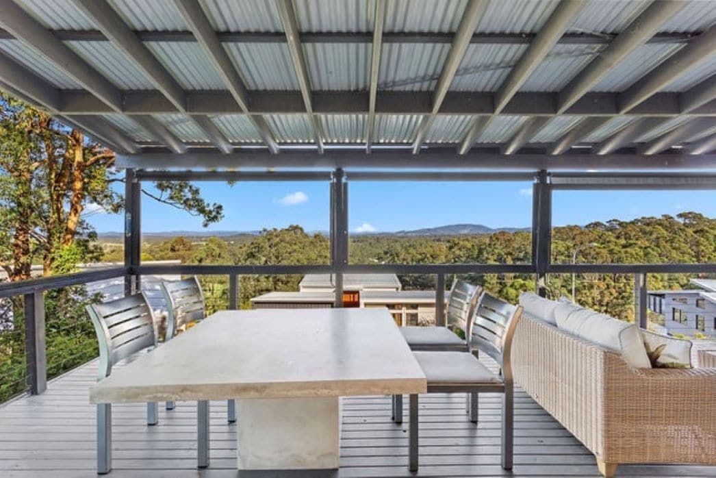 Un patio al aire libre con una mesa y sillas, con vistas a un paisaje de árboles y colinas.