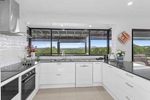 A modern kitchen with a large window, white cabinetry, and a stainless steel range hood.