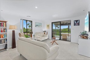 A modern living room with a sofa, coffee table, and bookshelf. There is a large window with a view of greenery.