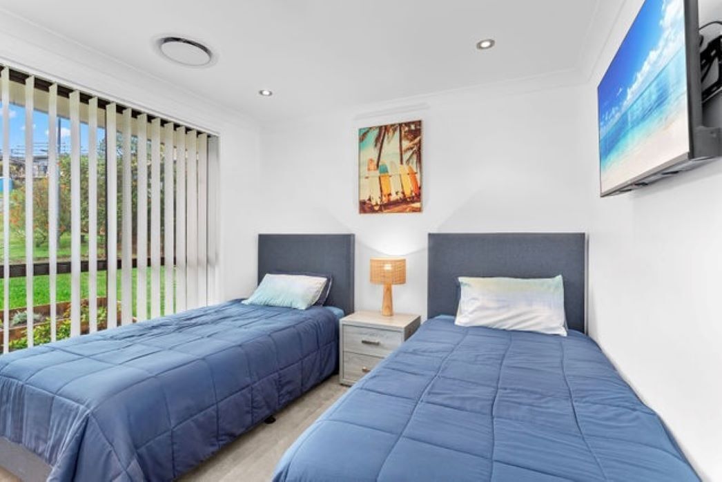 Un dormitorio con dos camas, una ventana con persianas, un cuadro y un televisor en la pared.