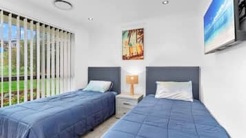 Un dormitorio con dos camas, una ventana con persianas, un cuadro y un televisor en la pared.