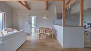 A modern interior with a wooden ceiling, a dining area with a table and chairs, a white sofa, and a kitchen area. - Adagio Retreat Tokachidake (Biei)