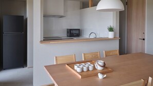 A modern kitchen with a microwave, sink, and wooden countertop. There is a dining table with chairs and a tray with cups and a teapot. - Adagio Retreat Tokachidake (Biei)