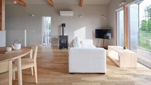 A spacious living area with a wooden floor, a sofa, a TV, and a fireplace. - Adagio Retreat Tokachidake (Biei)