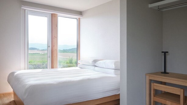 A bedroom with a bed, a desk, and a window with a view. - Adagio Retreat Tokachidake (Biei)