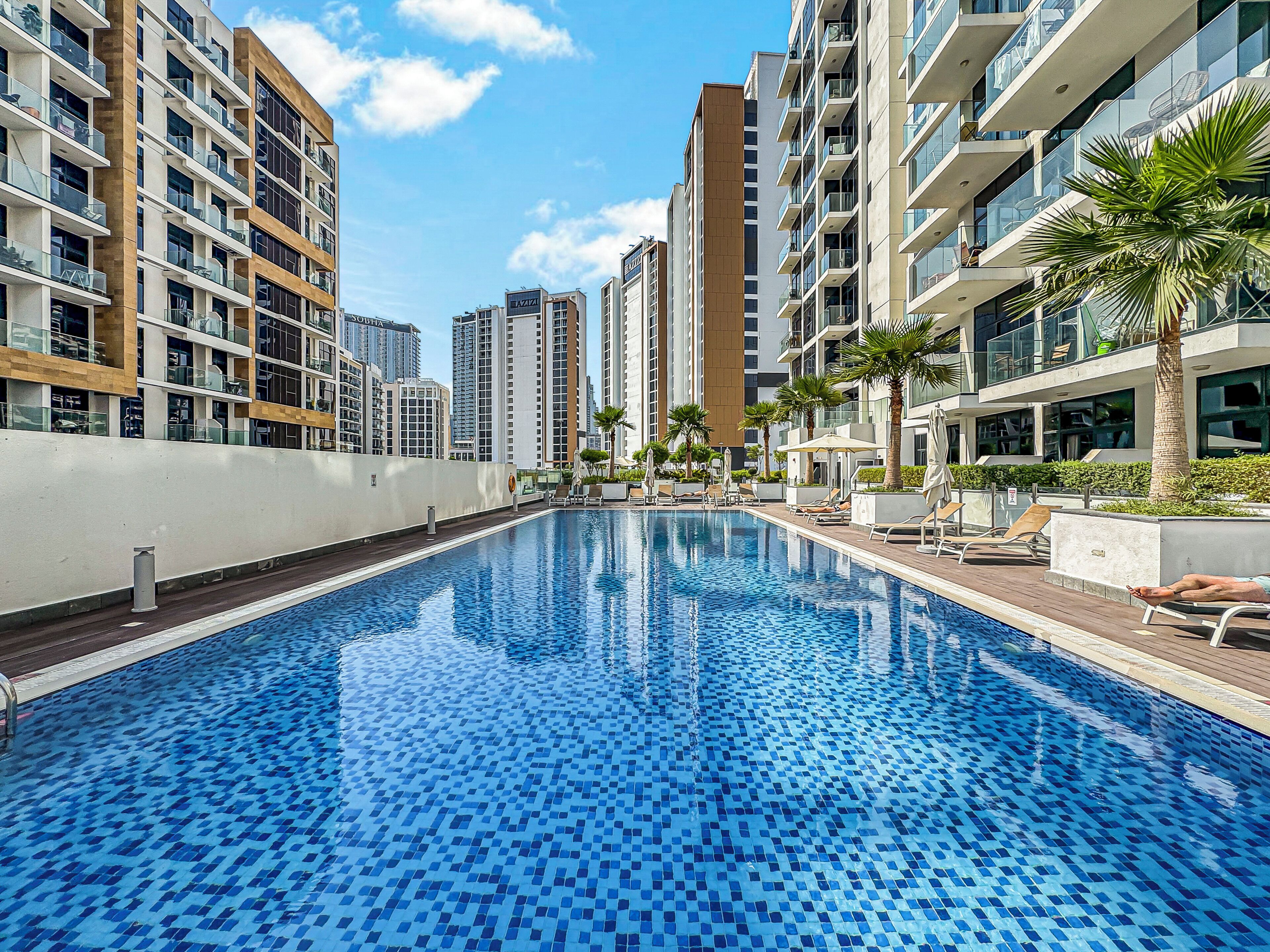 Una piscina con suelo de baldosas, rodeada de edificios residenciales altos, algunos con balcones.