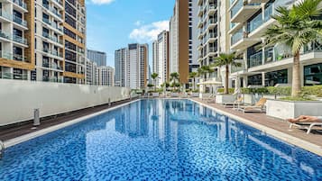 Una piscina con suelo de baldosas, rodeada de edificios residenciales altos, algunos con balcones.