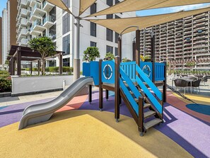 Ein Spielplatz mit Rutsche und Klettergerüsten, umgeben von einem Gebäude mit Balkonen und Außenplätzen.