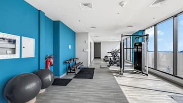 Un gimnasio moderno con equipo de ejercicio, un extintor y vistas al cielo a través de amplias ventanas.
