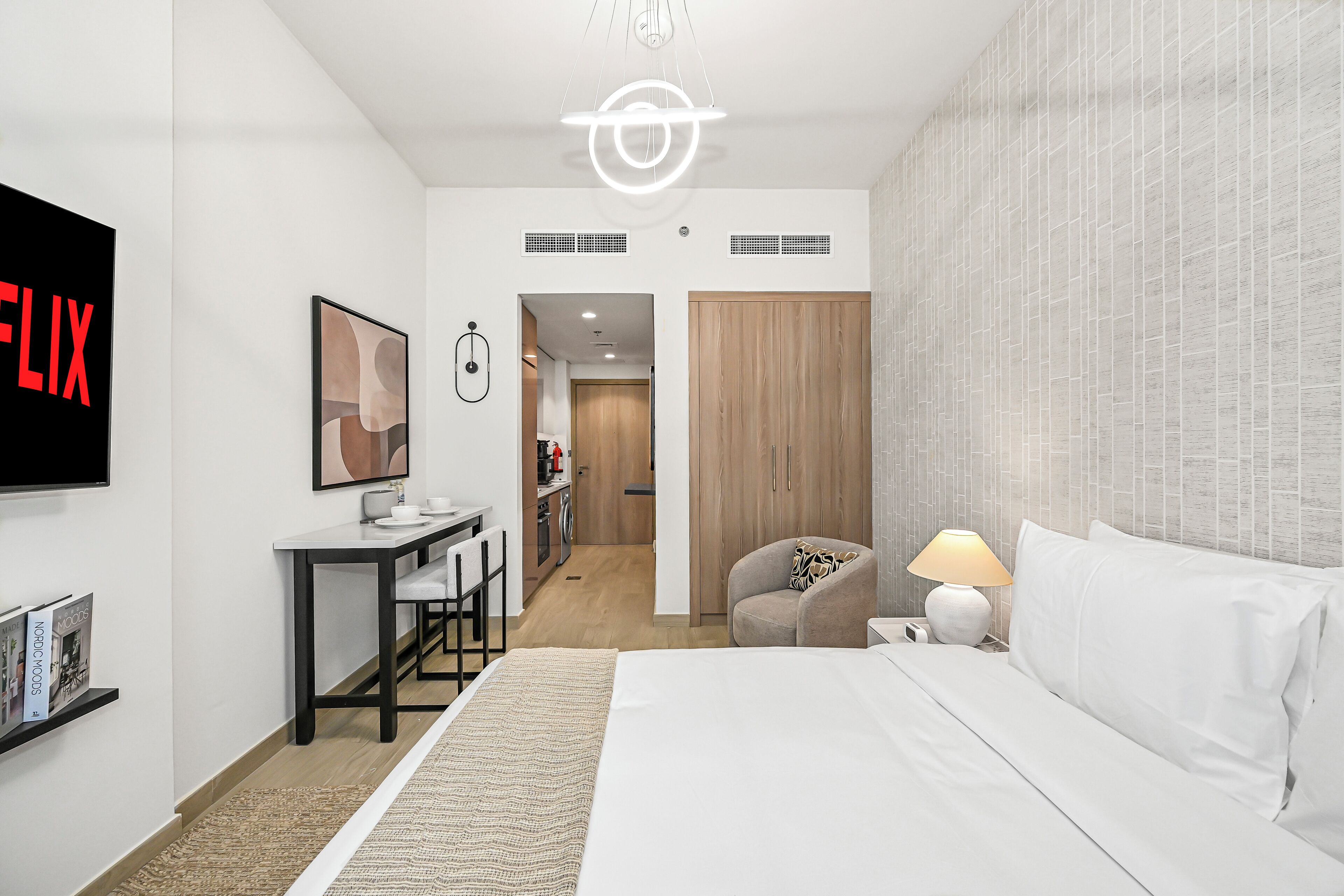 Una habitación de hotel moderna con cama, escritorio, silla, televisor y armario.
