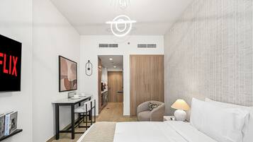 Una habitación de hotel moderna con cama, escritorio, silla, televisor y armario.