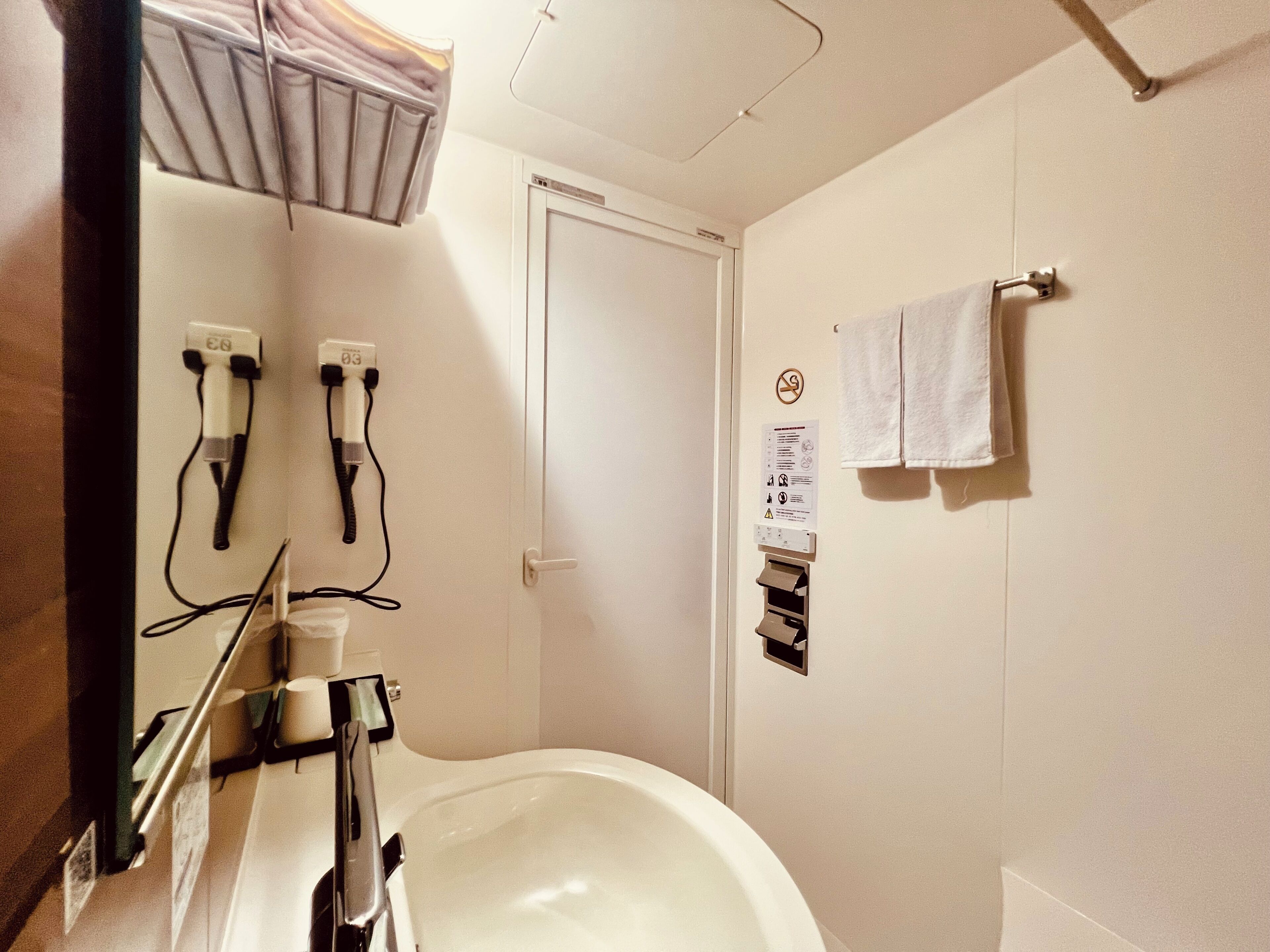 Une salle de bain équipée d’une baignoire, d’un porte-serviettes avec deux serviettes, d’un sèche-mains et d’une feuille contenant les consignes de sécurité.