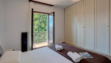 Ein Hotelzimmer mit einem Bett, einem Fenster mit Blick auf Grünflächen, einer Reihe weißer, schrägverlaufender Schränke und einer Zeitschrift auf dem Bett.